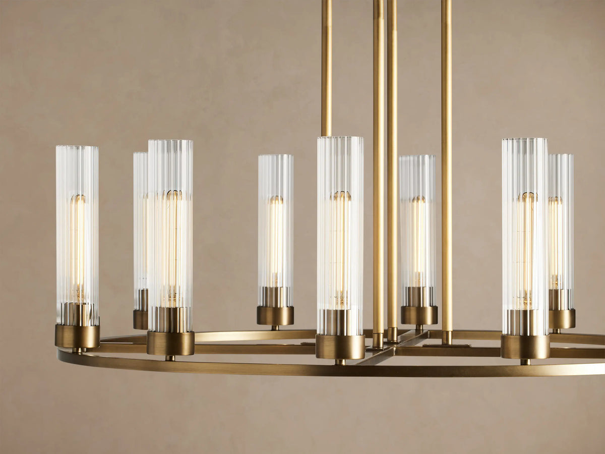 Gold-toned brass Andreas Round Chandelier with clear fluted glass cylinders holding bulbs, suspended from above.