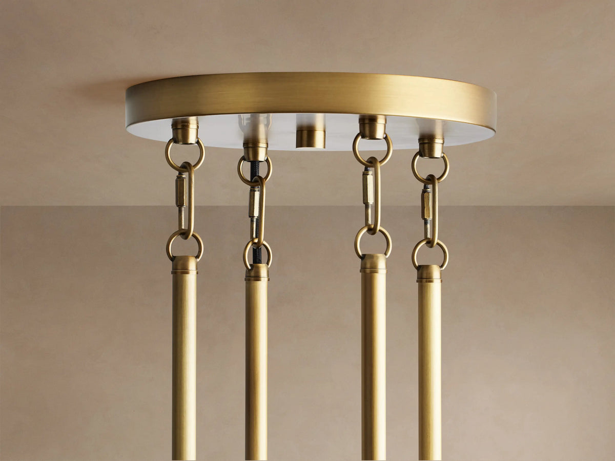 Andreas Round Chandelier, brass, with glowing filament bulbs visible in clear fluted glass cylinders.