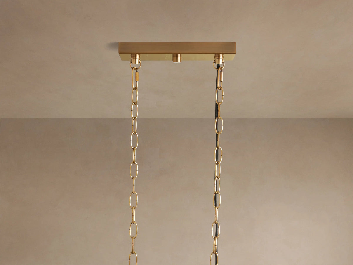 Close-up of Andreas Linear Chandelier with 5 warm-lit filament bulbs in fluted clear glass shades, brass finish.