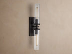 Andreas Double Sconce with two clear fluted glass shades, a dark bronze frame, and glowing exposed filament bulbs.