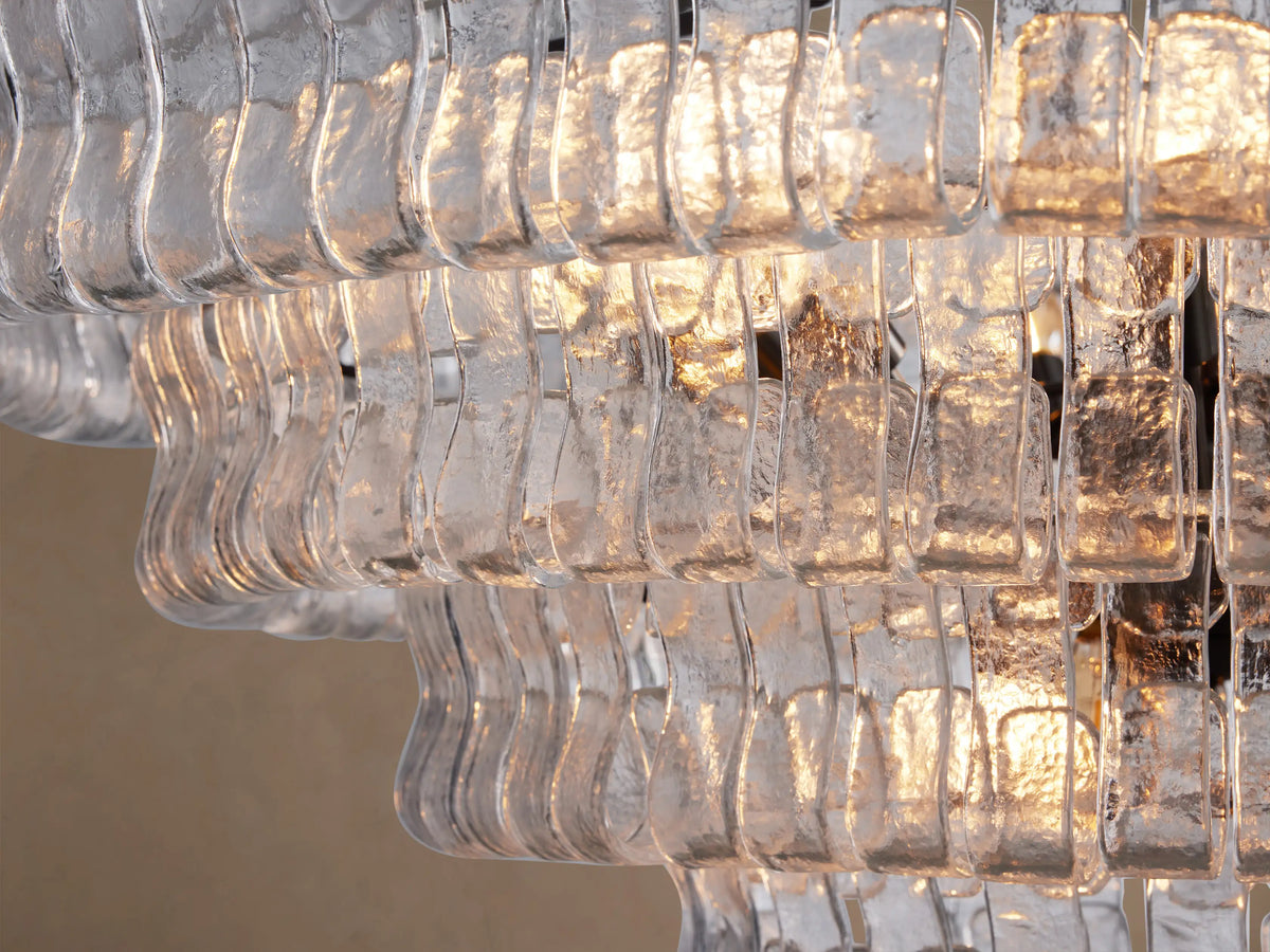 Close-up of Ghiaccio Round Chandelier with multiple layers of textured, curved clear glass panels glowing with warm light.