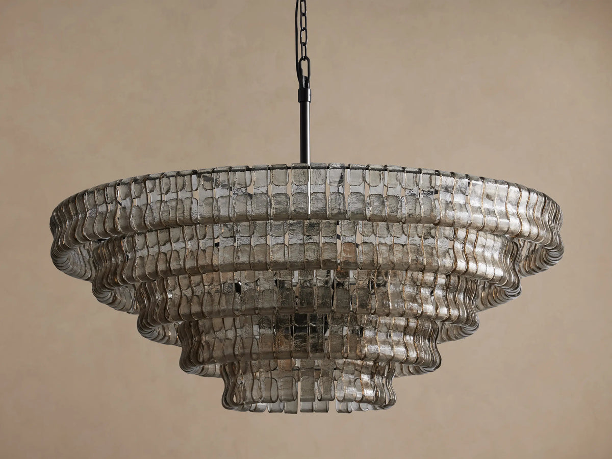Ghiaccio Round Chandelier, tiered, composed of wavy, rectangular clear glass pieces, suspended from a black chain against a beige wall.