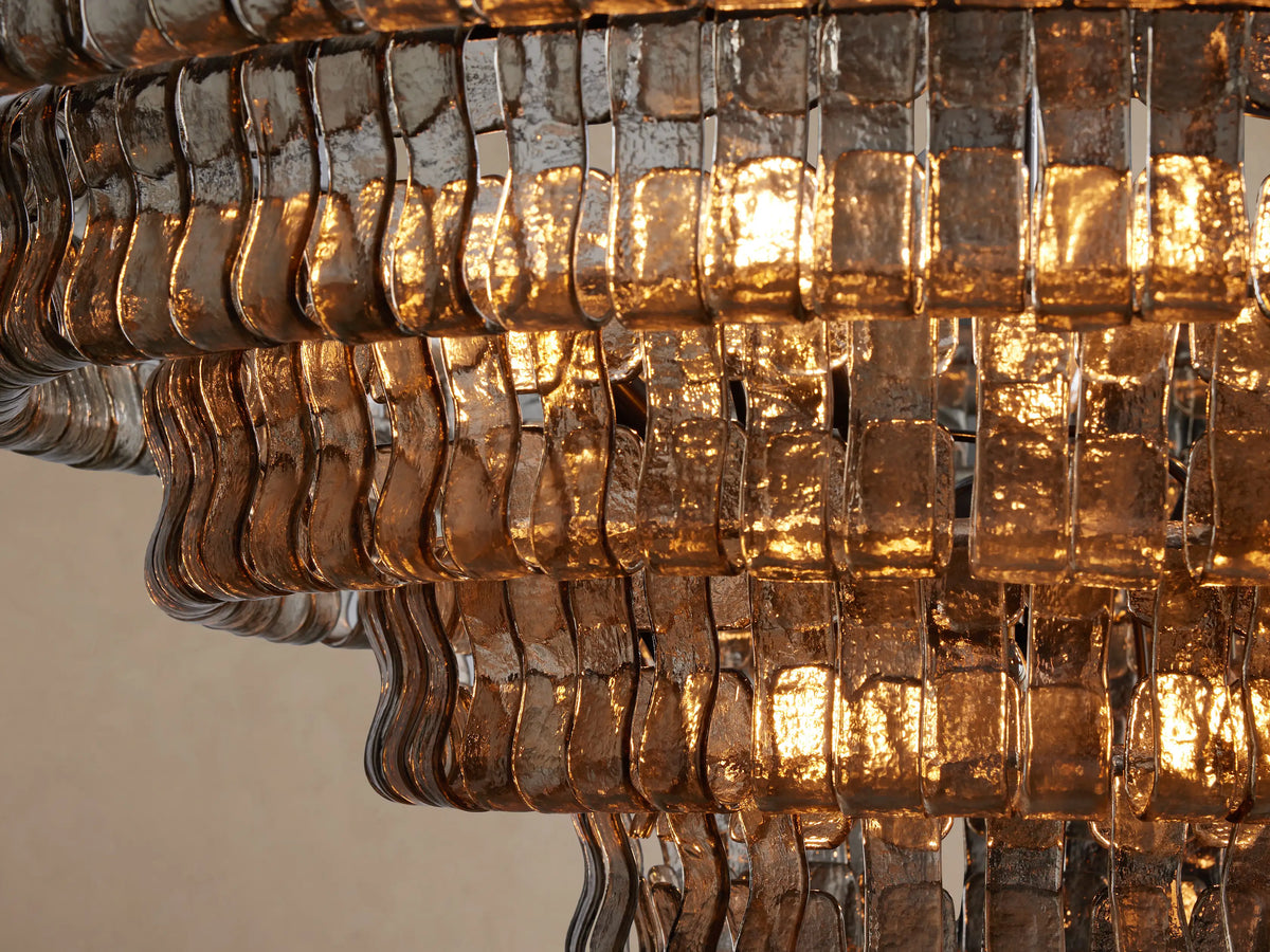 Close-up of a Ghiaccio Round Chandelier with multiple tiers of wavy, textured amber glass glowing with warm light.