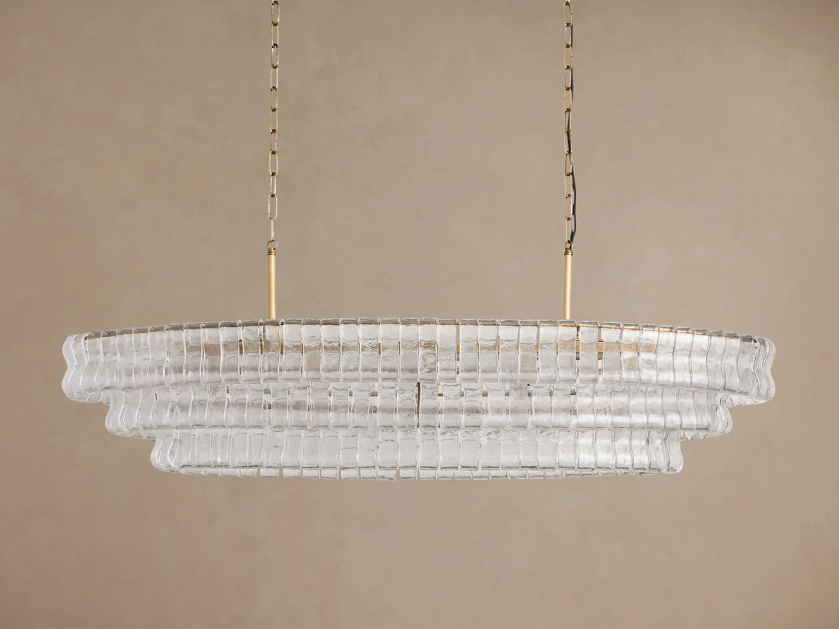 Ghiaccio Oval Chandelier with glowing lights, composed of tiered clear, curved glass segments, suspended by two golden chains.