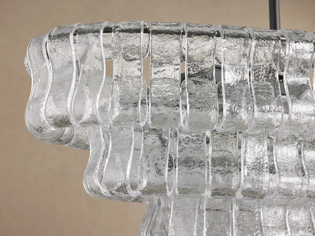 Front view of the Ghiaccio Oval Chandelier, featuring clear, tiered, textured glass segments and dark hanging chains.