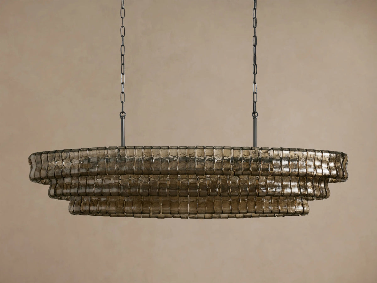 Ghiaccio Oval Chandelier with three tiers of textured, wavy, smoky glass panels, suspended by dark chains, glowing warmly.