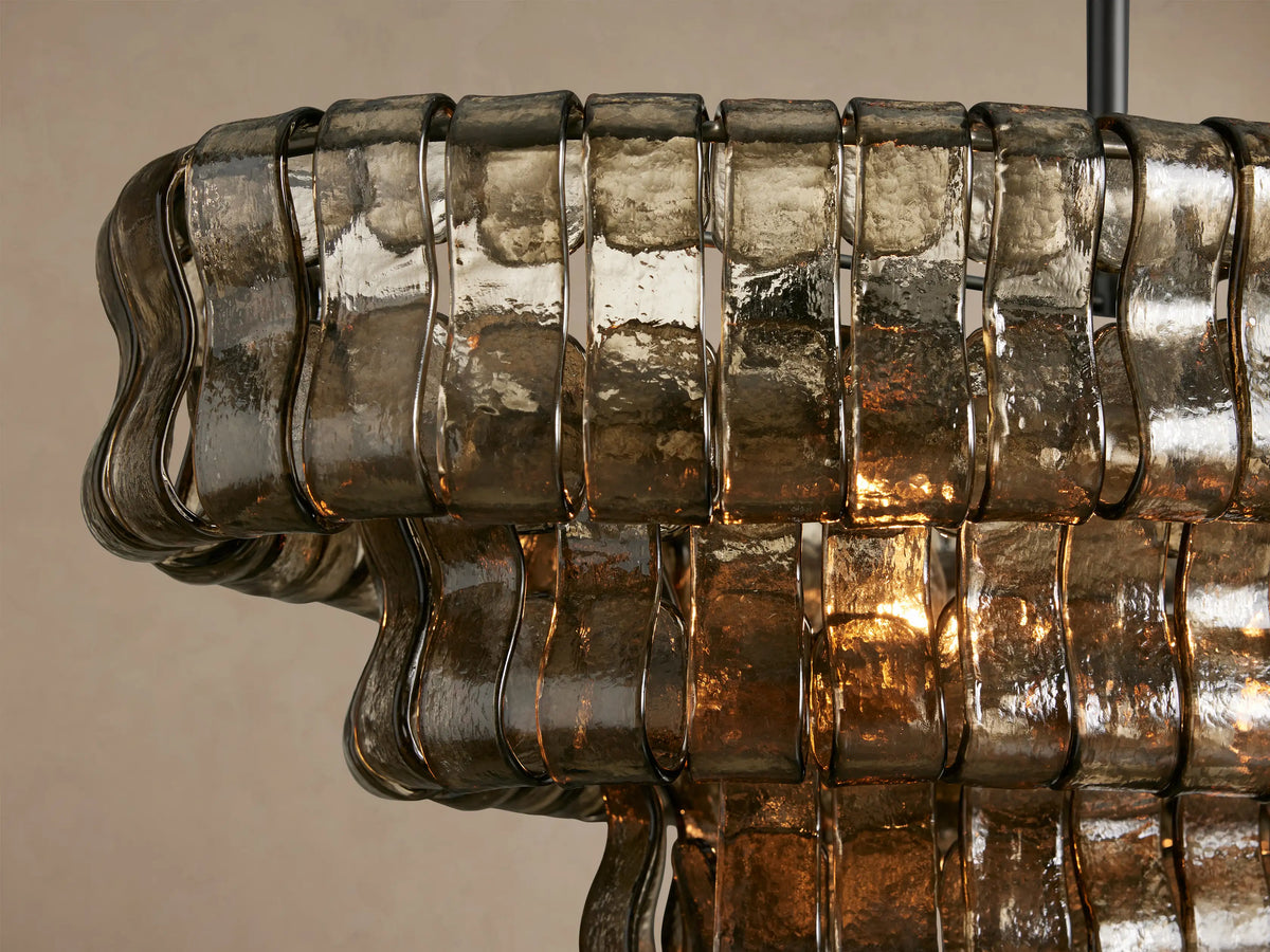 Ghiaccio Oval Chandelier features multiple layers of wavy, smoky brown glass panels, suspended by dark metal chains.
