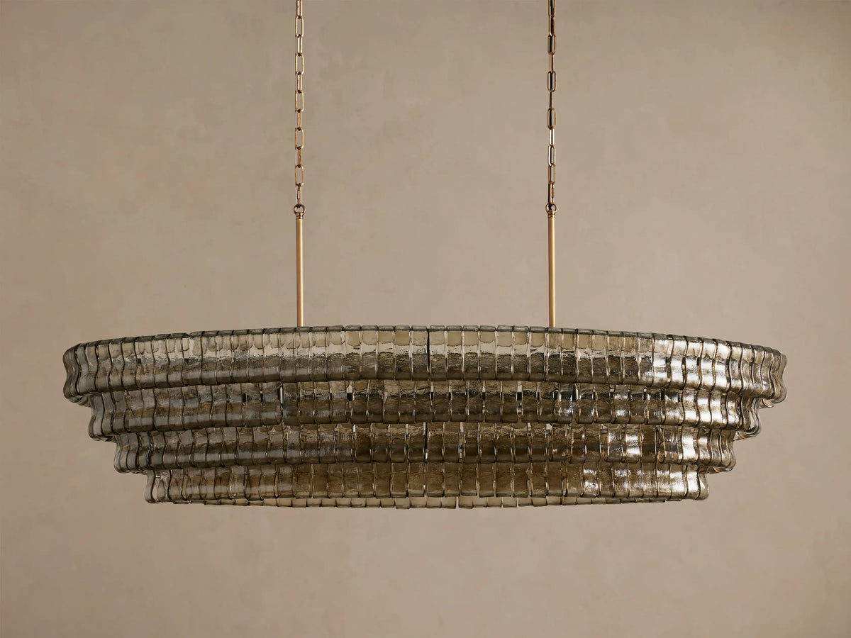 Ghiaccio Oval Chandelier. Oval chandelier with tiered, smoky textured glass and warm internal lighting, suspended by gold chains.