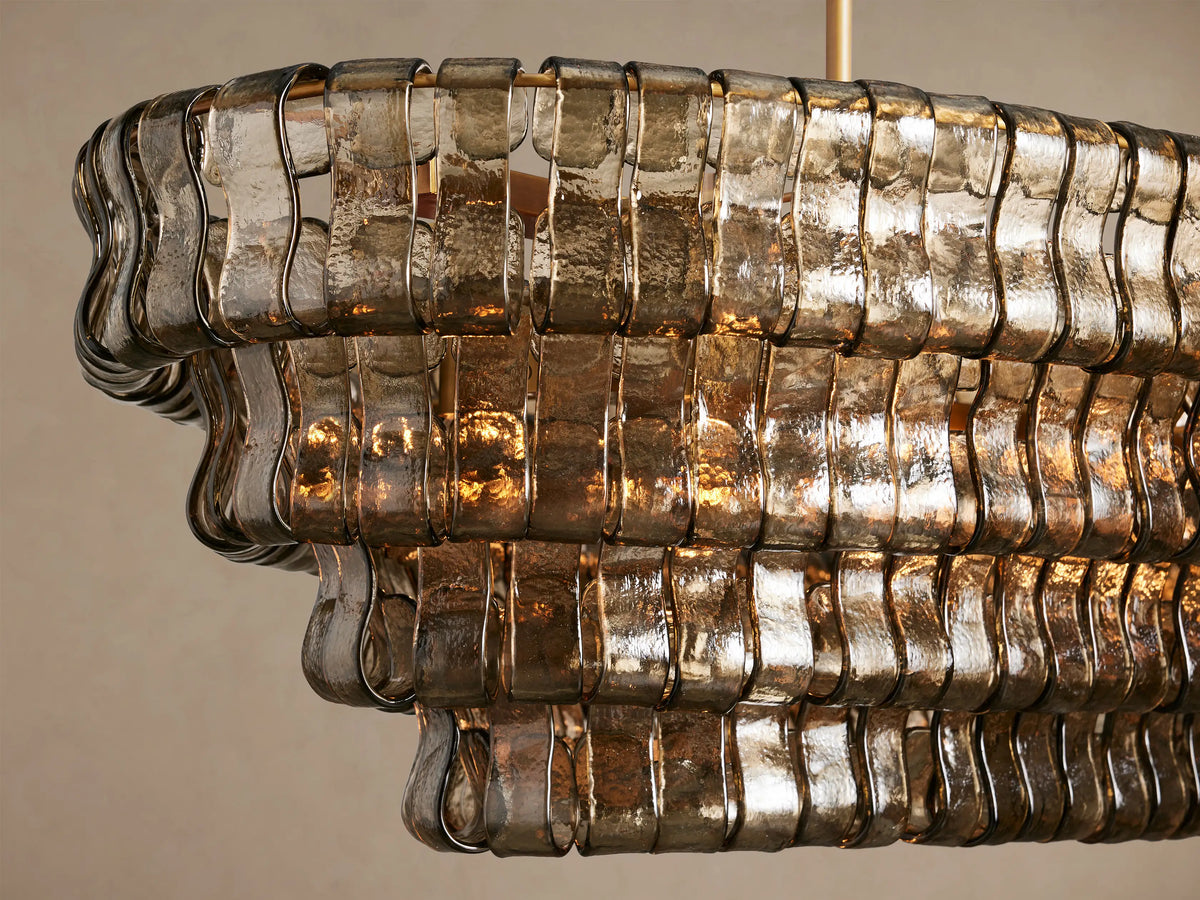 Ghiaccio Oval Chandelier with multi-tiered, textured smoky glass panels. Suspended by two gold chains against a neutral background.