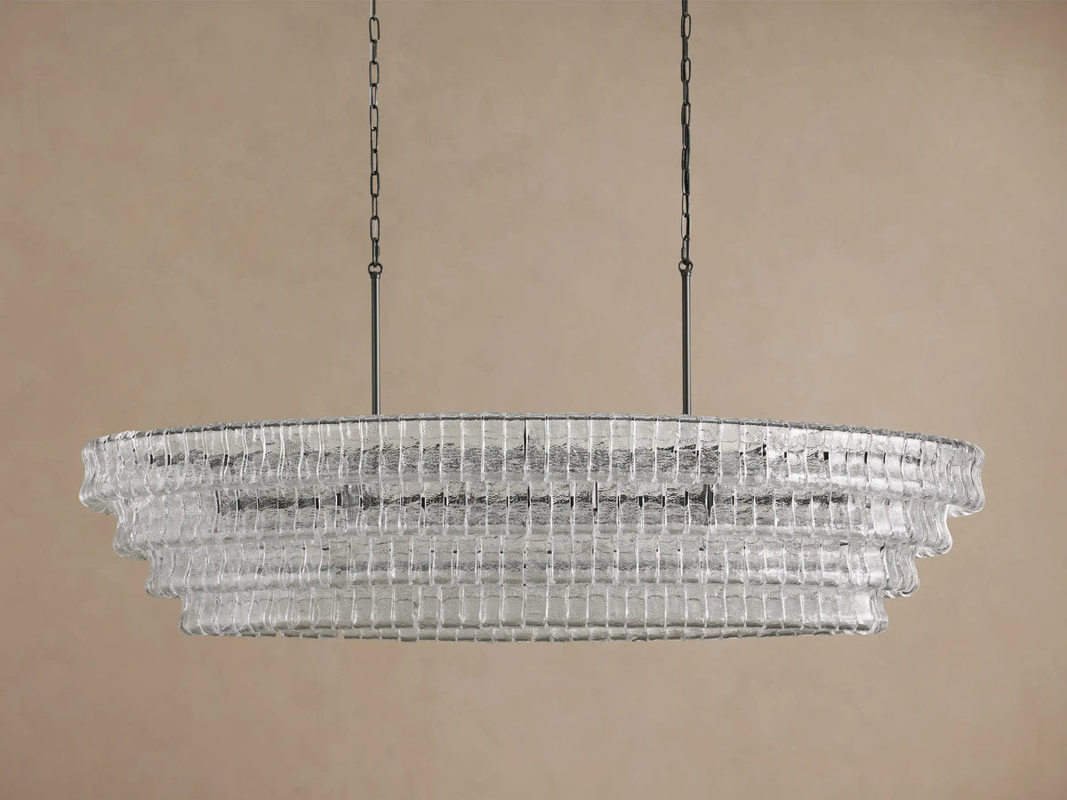 Illuminated Ghiaccio Oval Chandelier with layered, ribbed clear glass, suspended by dark chains against a neutral background.