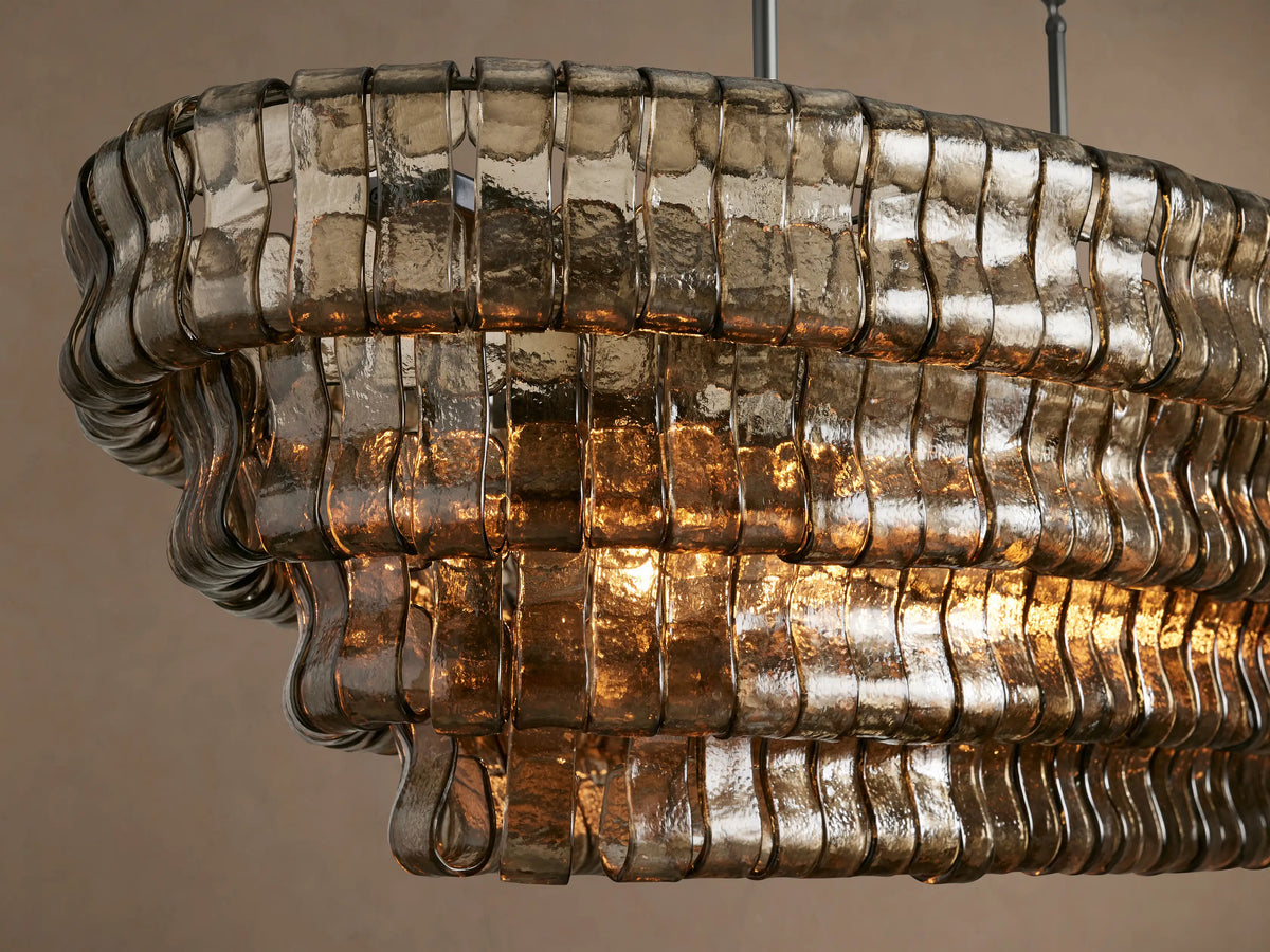 Ghiaccio Oval Chandelier, a large oval chandelier with multiple descending layers of textured, smoky amber glass suspended by dark chains.