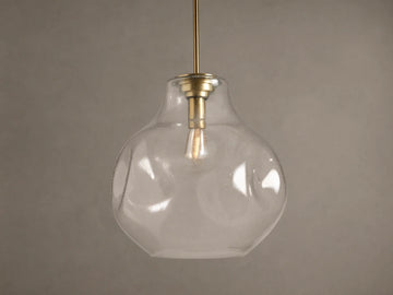 Organic 16" Pendant: Clear, seeded mouth-blown glass shade, brass stem, glowing filament bulb, against a brown wall.