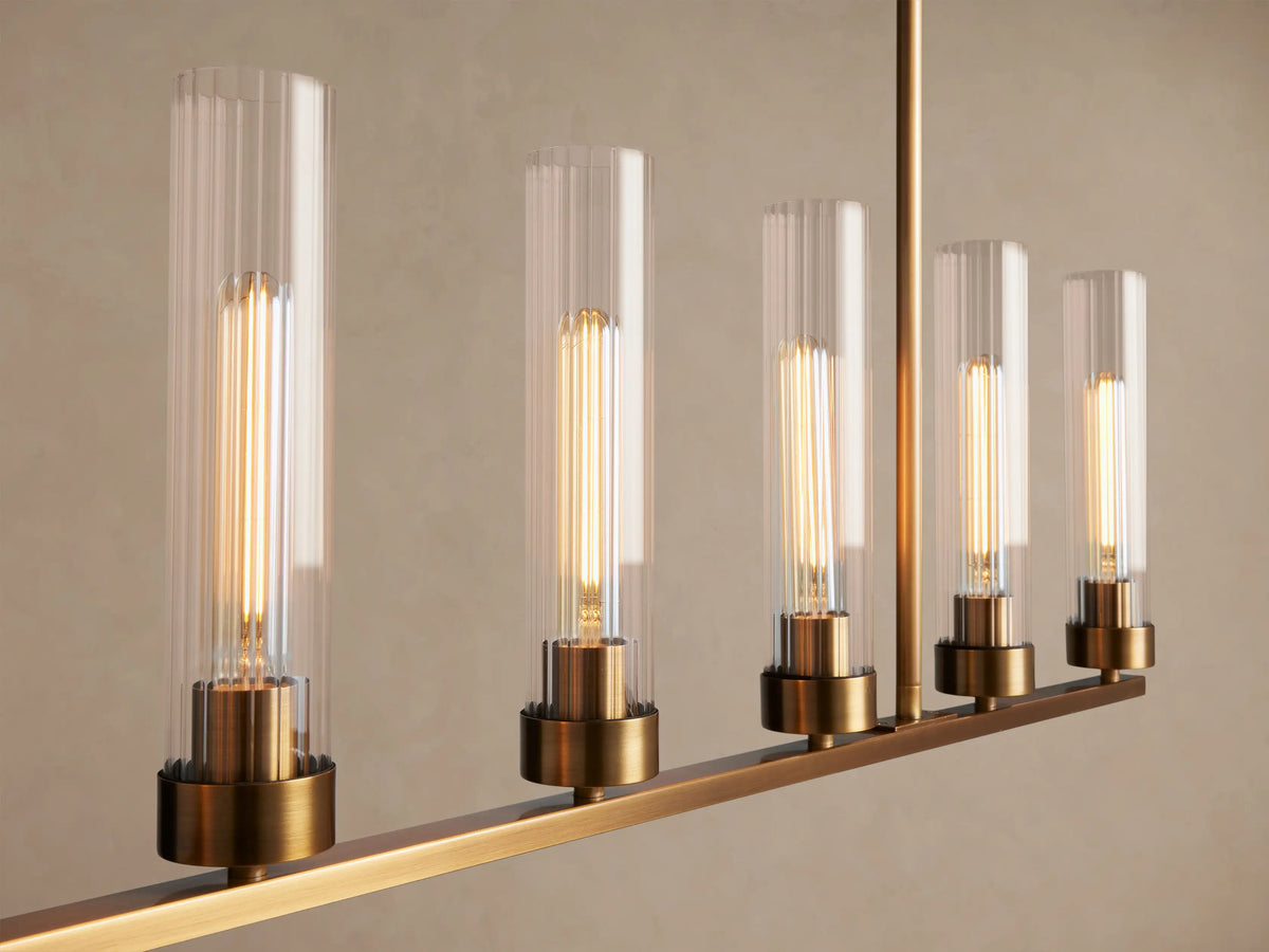Andreas Linear Chandelier: 8 clear glass cylinder lights over brass frame, suspended by chains & rods against a neutral wall.