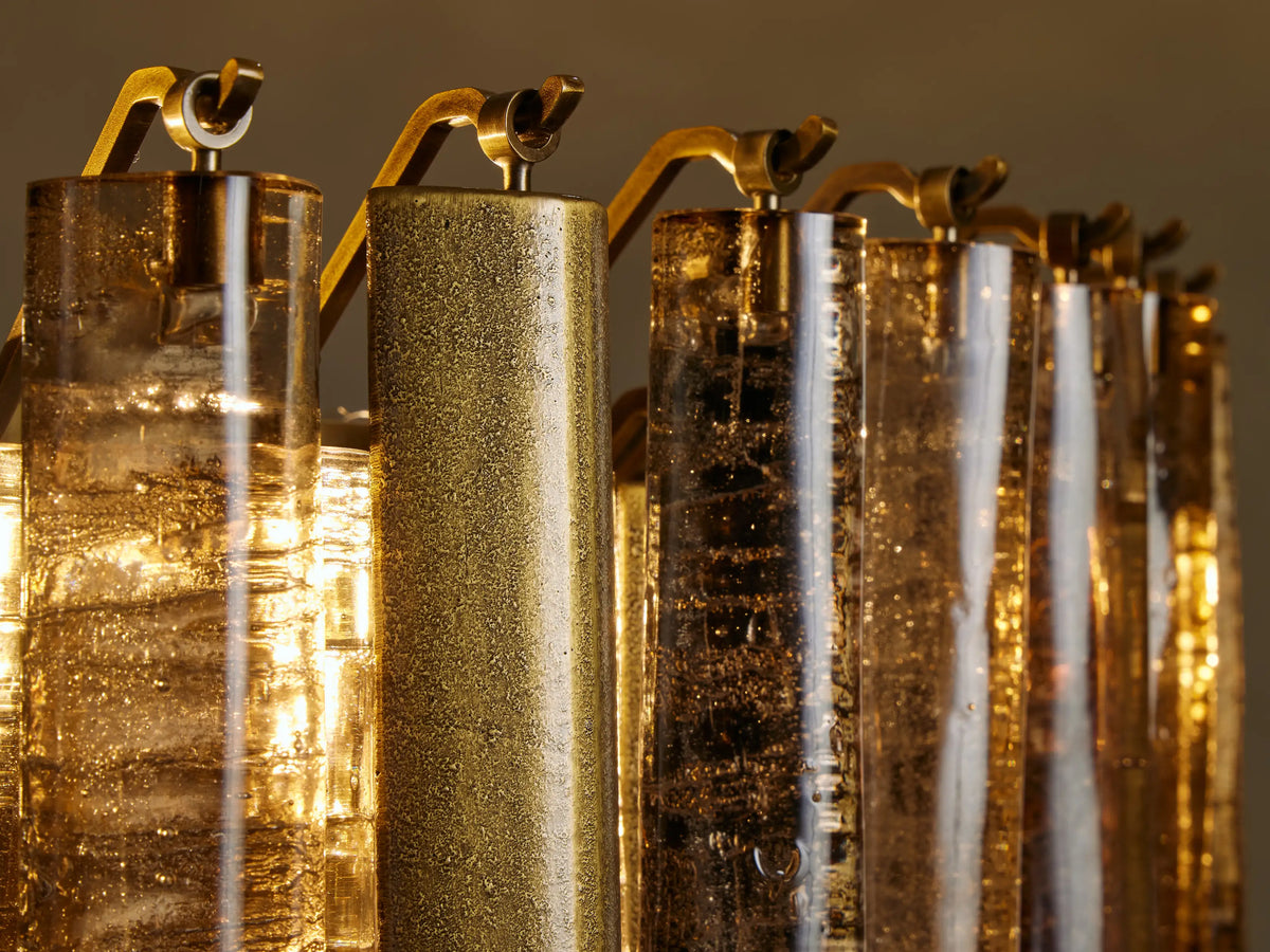 Neve Round Chandelier close-up: Alternating textured bronze glass & brass aluminum cylinders, glowing warmly.