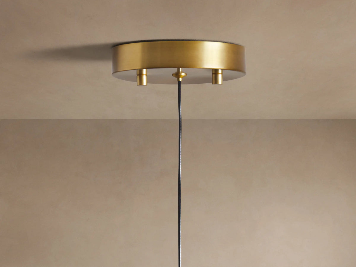 Soltaire Pendant: Close-up of a brass-topped, clear teardrop glass pendant light with illuminated bubbles inside, glowing warmly.