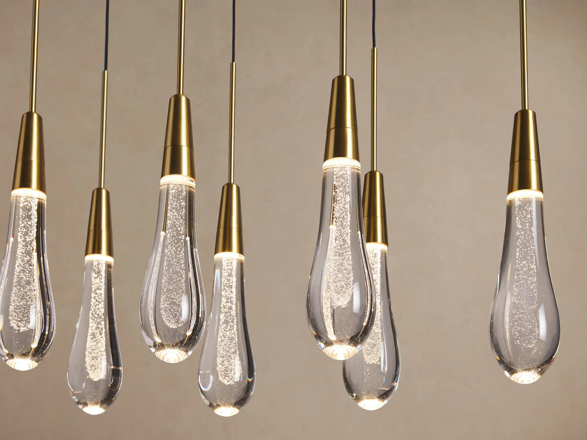 Soltaire Linear Chandelier with multiple teardrop clear glass pendants, brass-finished tops, and sparkling internal lights.