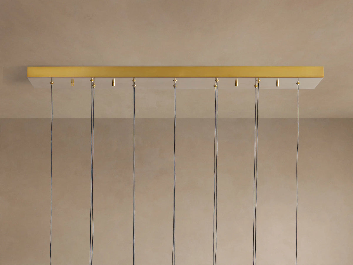 Soltaire Linear Chandelier showing its gold-finished linear canopy mounted to a light ceiling, with multiple black cords hanging.