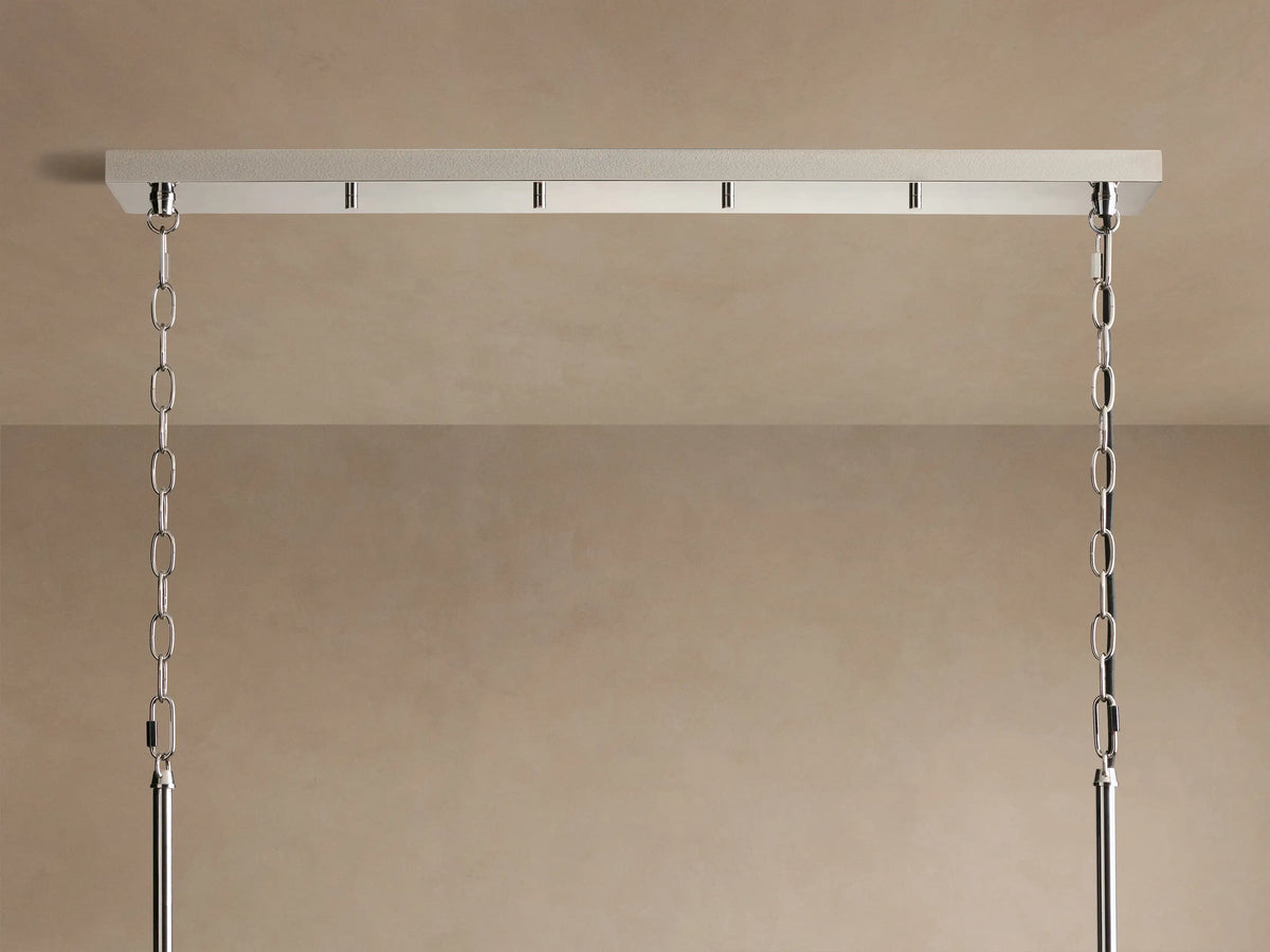 Andreas Linear Chandelier, polished chrome finish, featuring four fluted glass cylinders with visible filament bulbs against a tan wall.