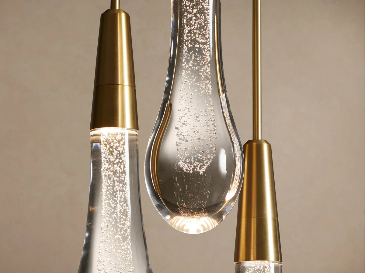 Close-up of Soltaire Round Chandelier with brass tops & clear, bubble-filled glass drops illuminated warmly on a soft background.
