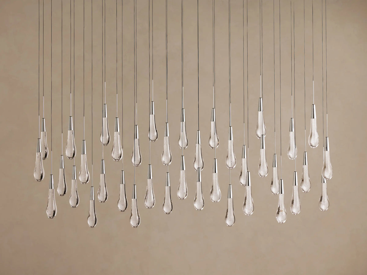 Soltaire Linear Chandelier with many sparkling clear teardrop glass pendants hanging vertically from thin wires, metallic accents.