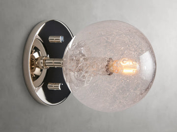Mandoza Sconce with polished nickel-finished steel base featuring a textured hand-blown glass globe, mounted on a wall.