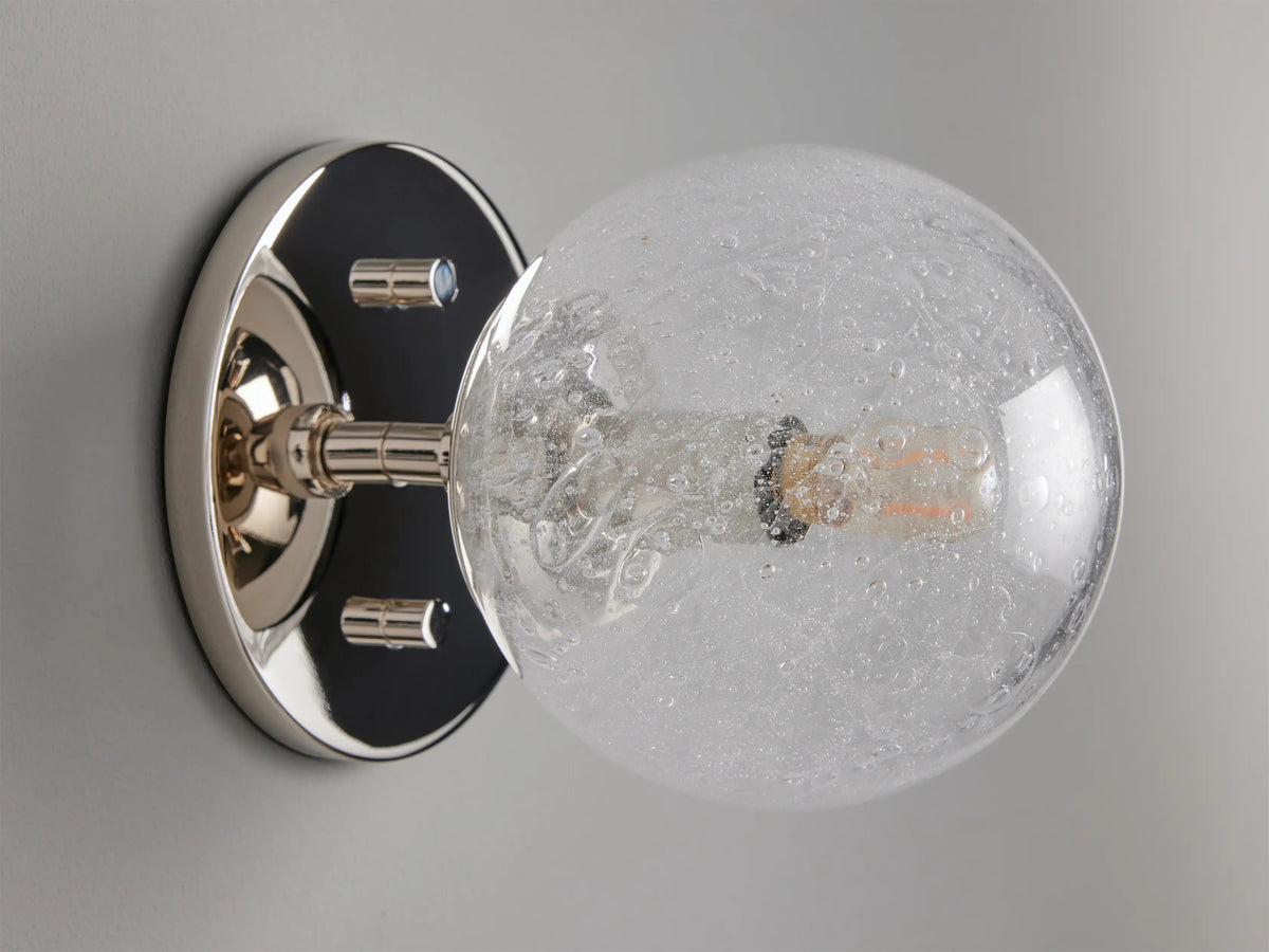 Mandoza Sconce with polished nickel-finished steel base featuring a textured hand-blown glass globe, mounted on a wall.