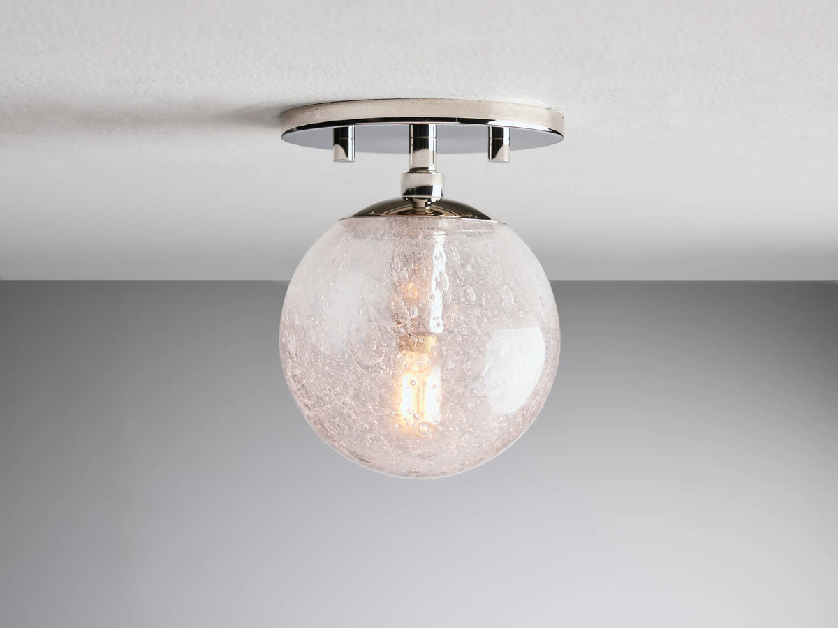 Mandoza Sconce with polished nickel-finished base, clear hand-blown glass globe, visible filament bulb, mounted on a wall.