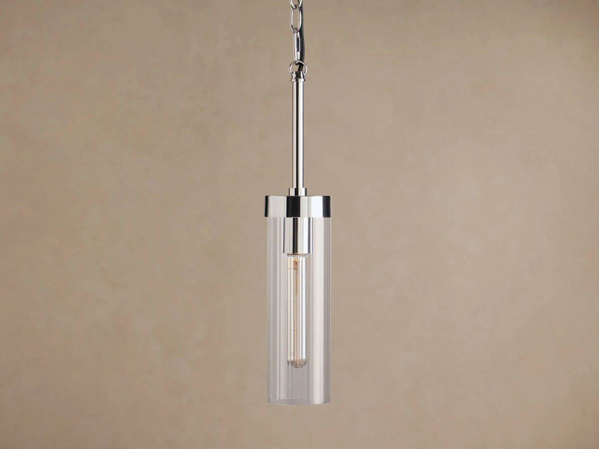 Andreas Pendant, polished nickel with clear cylindrical glass shade and vintage-style filament bulb, hanging from chain and rod against brown.