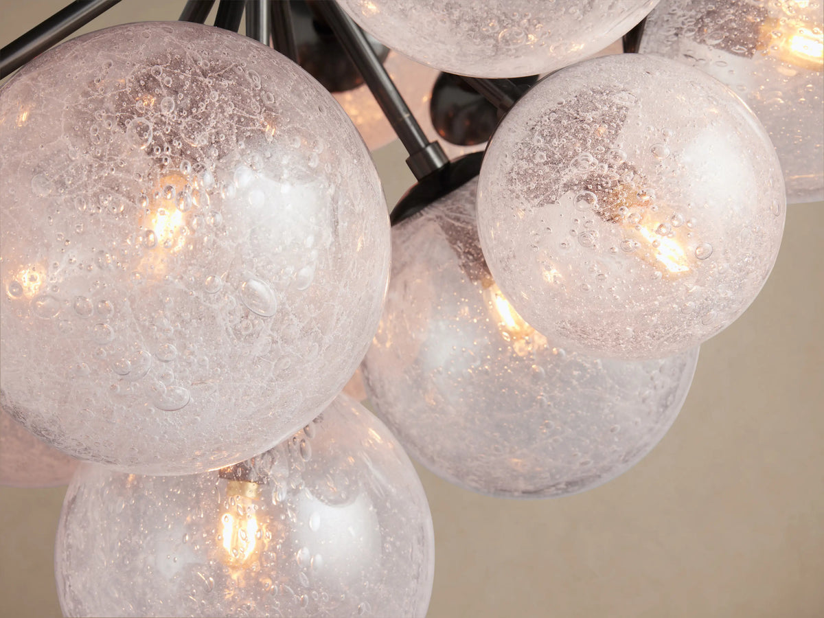 Close-up of Mandoza Chandelier featuring multiple hand-blown clear glass globes with a bubbly texture, each lit by warm LED filament bulbs, against dark metal arms.