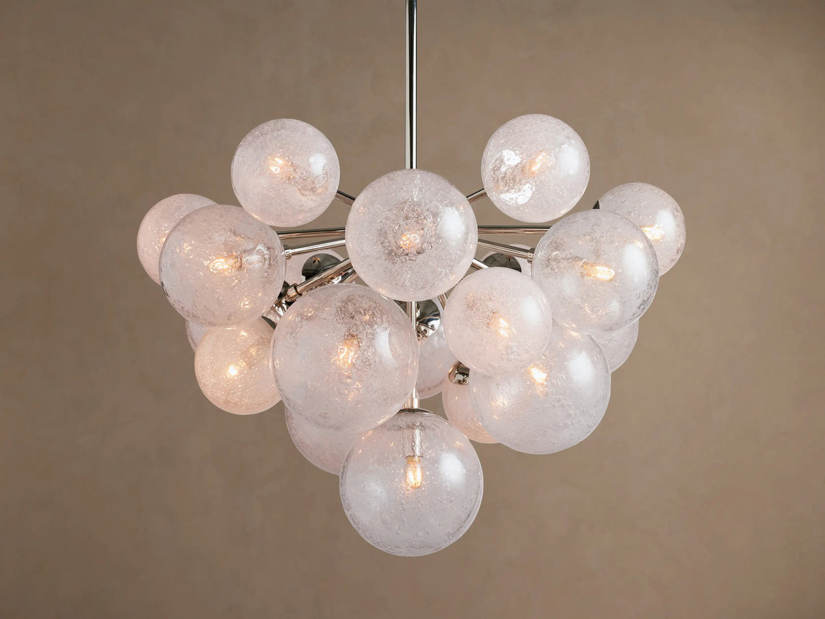 Mandoza Chandelier: Clustered, illuminated textured glass globes on a polished nickel frame, centered against a warm beige wall.