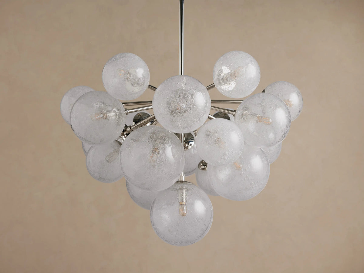Mandoza Chandelier: Clustered, illuminated textured glass globes on a polished nickel frame, centered against a warm beige wall.