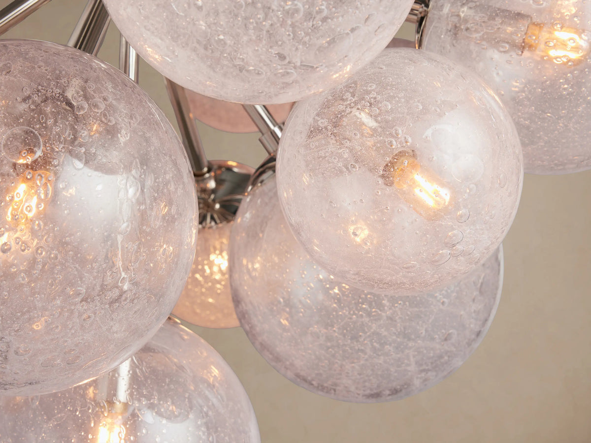 Mandoza Chandelier: Polished nickel fixture with many textured clear glass globes and visible bulbs, hanging against a beige wall.