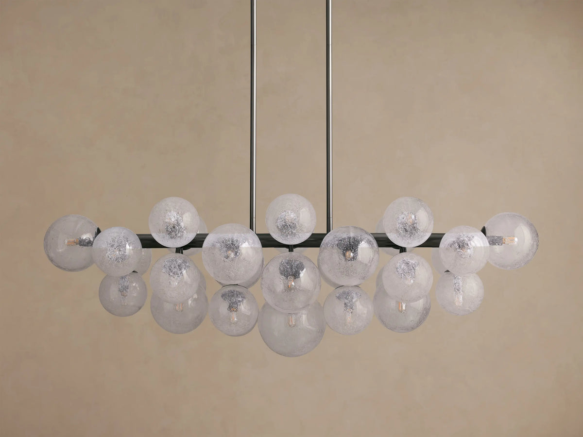 Mandoza Linear Chandelier with a burnished brass frame holding multiple illuminated, speckled hand-blown glass globes.