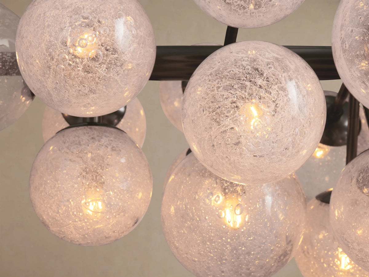 Mandoza Linear Chandelier with a dark metal linear frame and multiple clear, frosted glass globes against a beige wall.