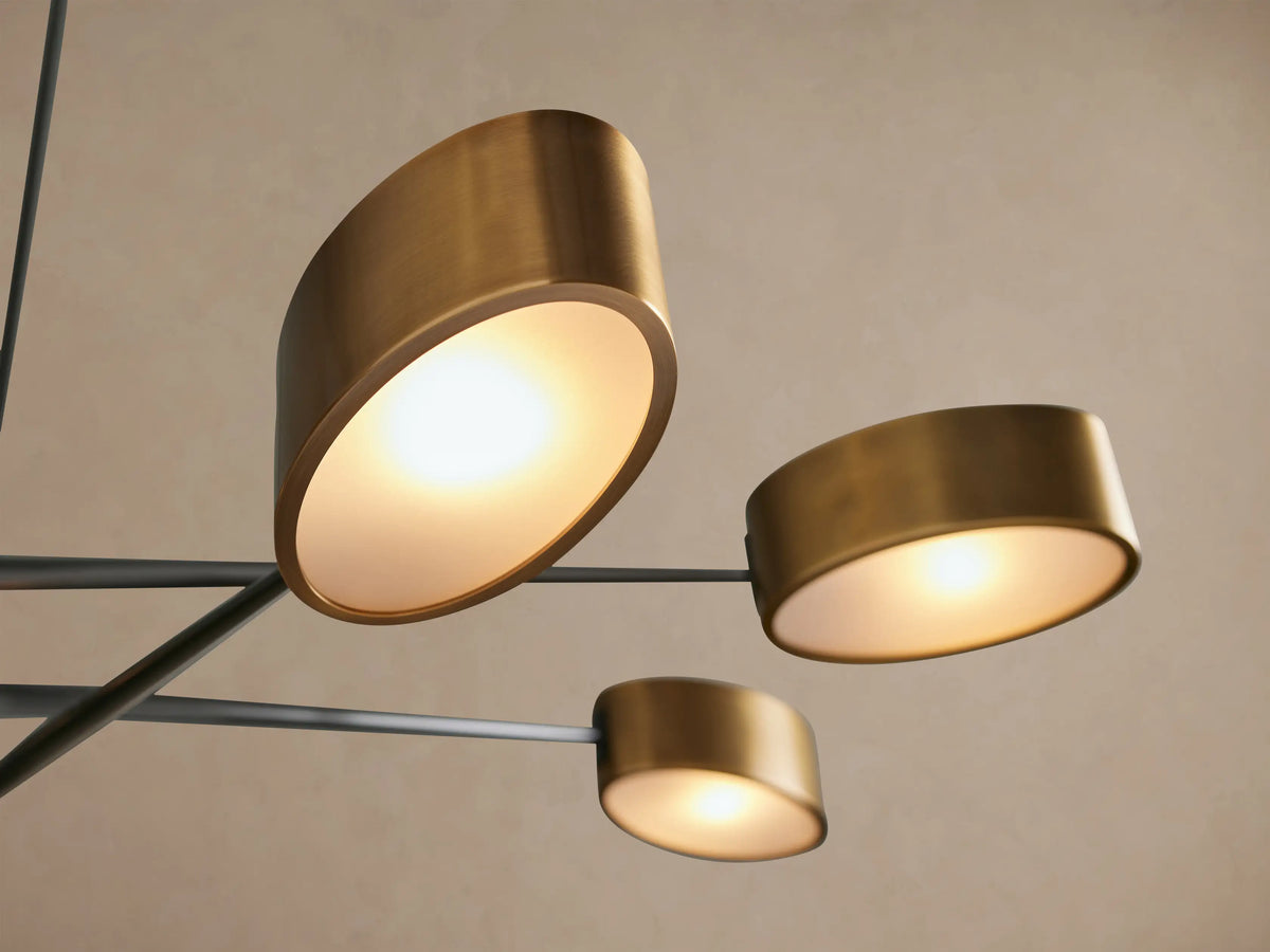 Etoile Chandelier: Modern six-light fixture with black angled arms and cylindrical brass shades, hanging against a plain wall.