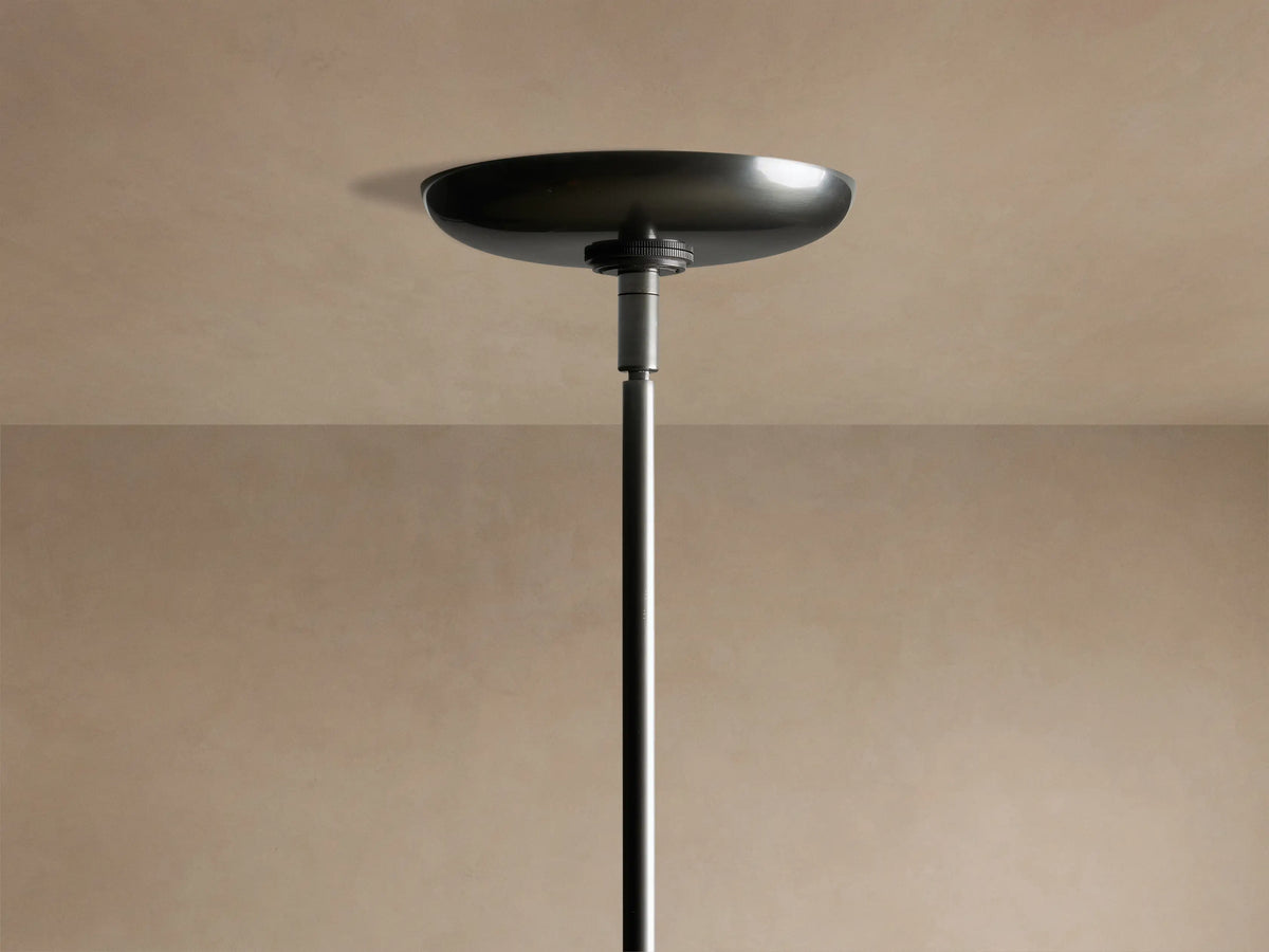 Close-up of Etoile Chandelier, showing three illuminated brass and bronze shades on dark grey arms, glowing on beige background.
