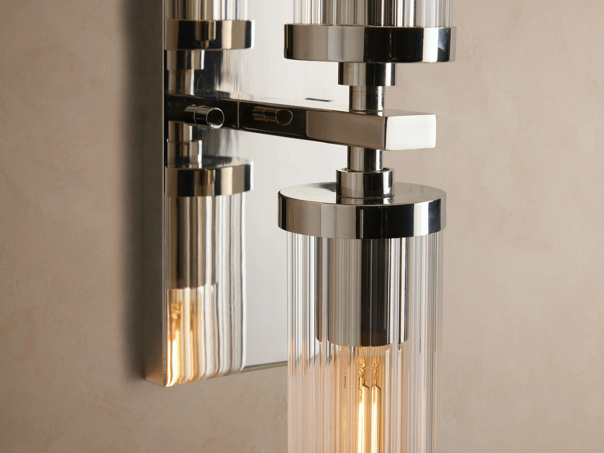 Andreas Double Sconce: polished nickel, two vertical clear ribbed glass shades, visible filament bulbs on a beige wall.