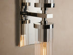 Andreas Double Sconce: polished nickel, two vertical clear ribbed glass shades, visible filament bulbs on a beige wall.