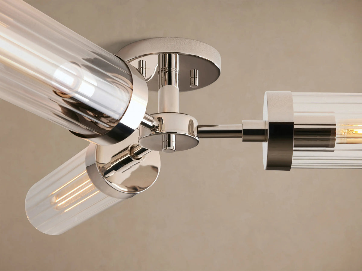 Polished nickel Andreas Flush Mount with 3 clear cylindrical glass shades, visible filament bulbs, mounted on a light brown ceiling.
