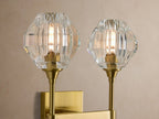 Amoroso Double Sconce with two faceted crystal shades & brass-plated arms, mounted vertically on a light beige wall.
