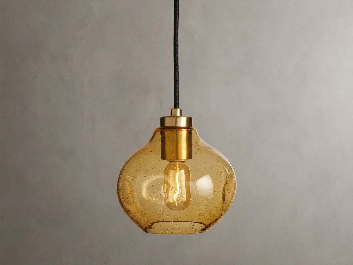 Organic 8" Pendant with amber mouth-blown glass shade, showing a visible filament bulb, suspended by a black fabric cord against a neutral background.