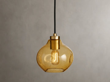 Organic 8" Pendant with amber mouth-blown glass shade, showing a visible filament bulb, suspended by a black fabric cord against a neutral background.