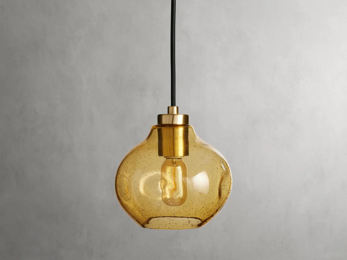Organic 8" Pendant with amber mouth-blown glass shade, showing a visible filament bulb, suspended by a black fabric cord against a neutral background.