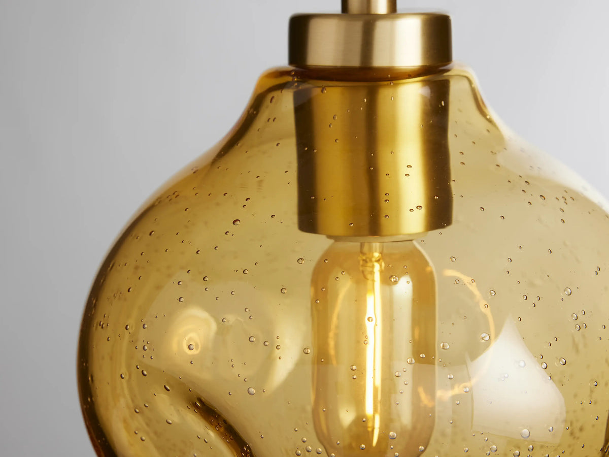Organic 8" Pendant with amber, mouth-blown glass shade and black cord, featuring brass hardware. Bulb visible inside.