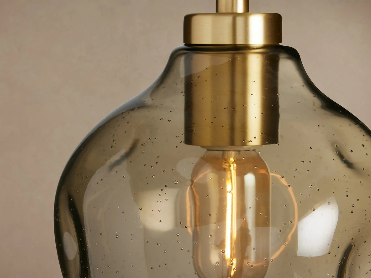 Organic 8" Pendant, an irregular smoky grey speckled glass shade with brass hardware, clear filament bulb, hanging from black cord.