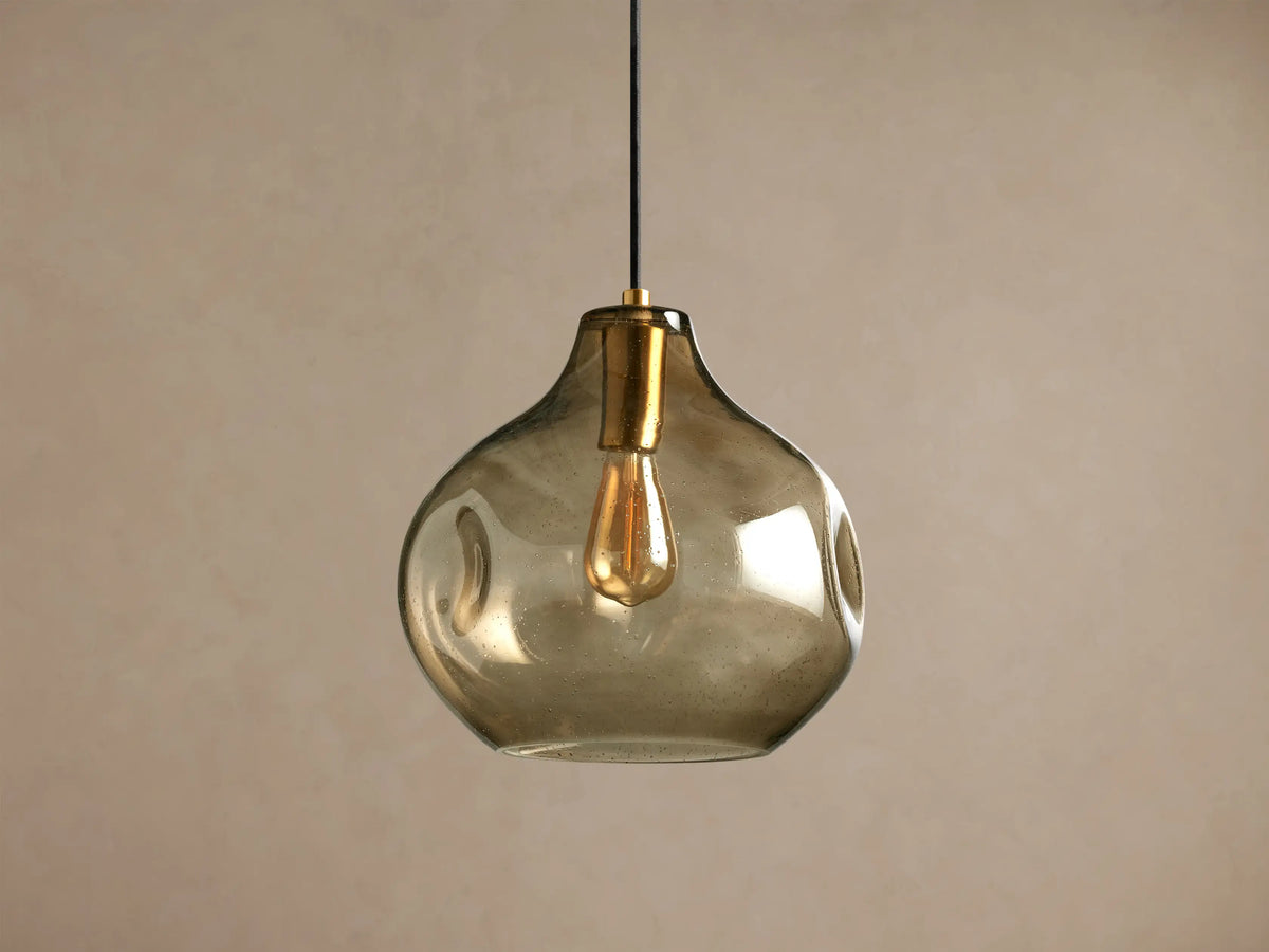 Organic 12" Pendant with smoky gray mouth-blown glass shade, brass fitting, glowing Edison bulb, black cord, hanging.