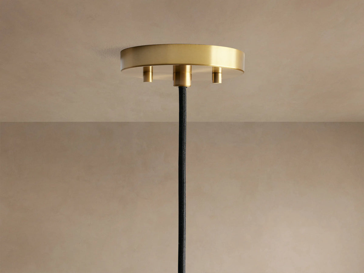 Close-up of Organic 12" Pendant's gold circular ceiling mount and black fabric-wrapped cord on a tan ceiling.