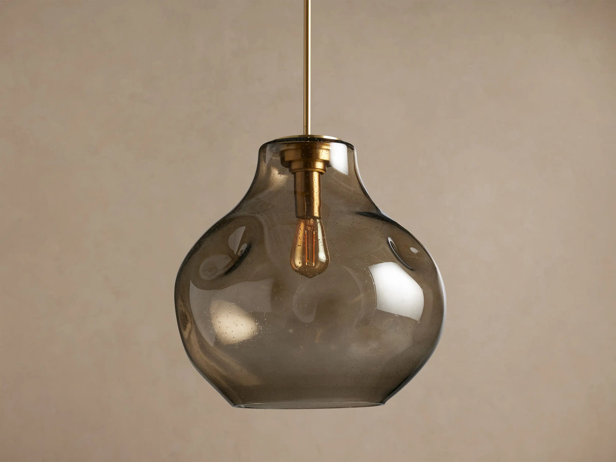 Organic 16" Pendant: Irregular, smoky, seeded glass shade with brass hardware, housing a glowing filament bulb, hanging.