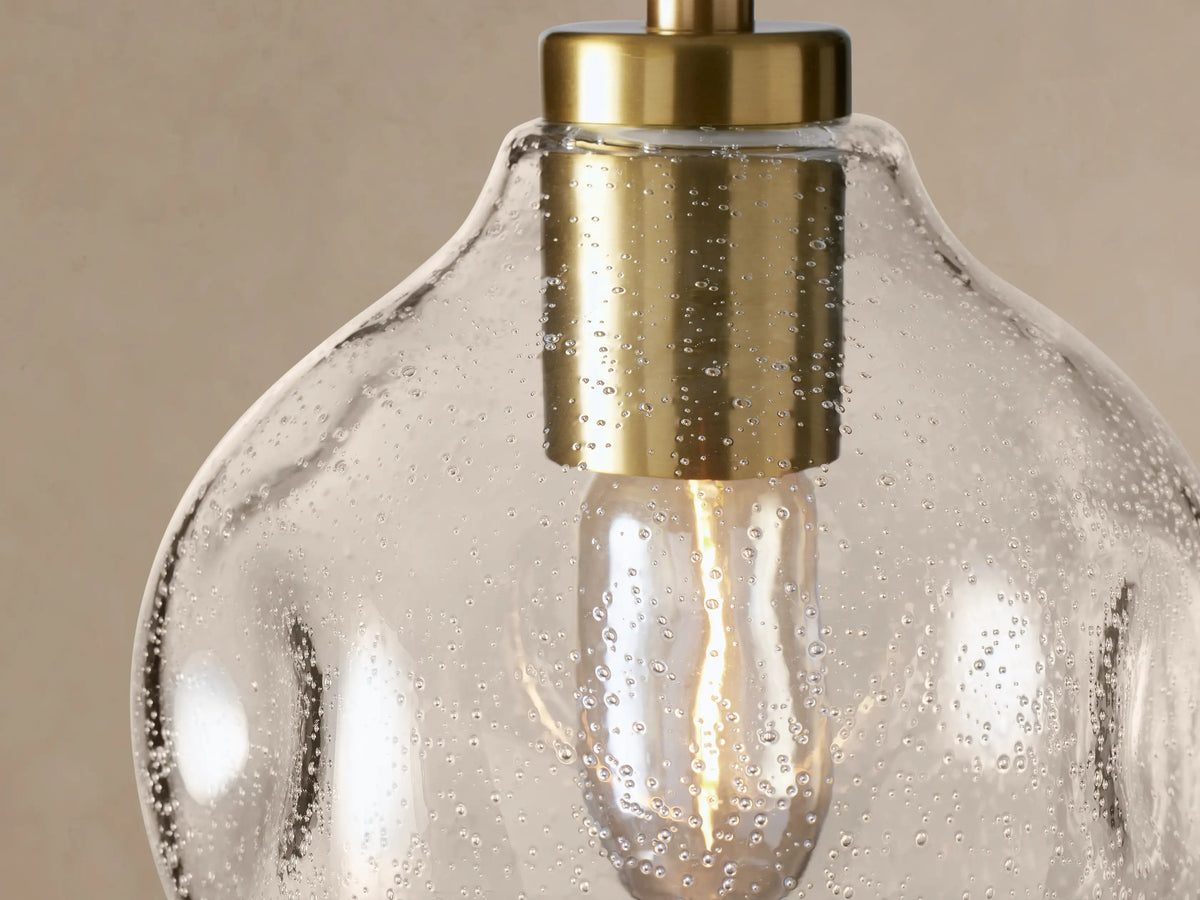 Organic 8" Pendant: Clear, seeded mouth-blown glass bulb-shaped pendant with brass fitting and black cord, against a light wall.