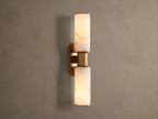 Harlin Double Sconce: Two glowing alabaster cylinder shades with burnished brass trim, mounted vertically on a neutral wall.